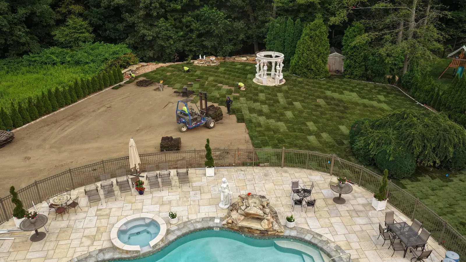 Drone view over the pool patio of a Shelton, CT estate as the CT Sod crew lays fresh farm-cut sod around the columned gazebo — a full backyard lawn taking shape in a single day.