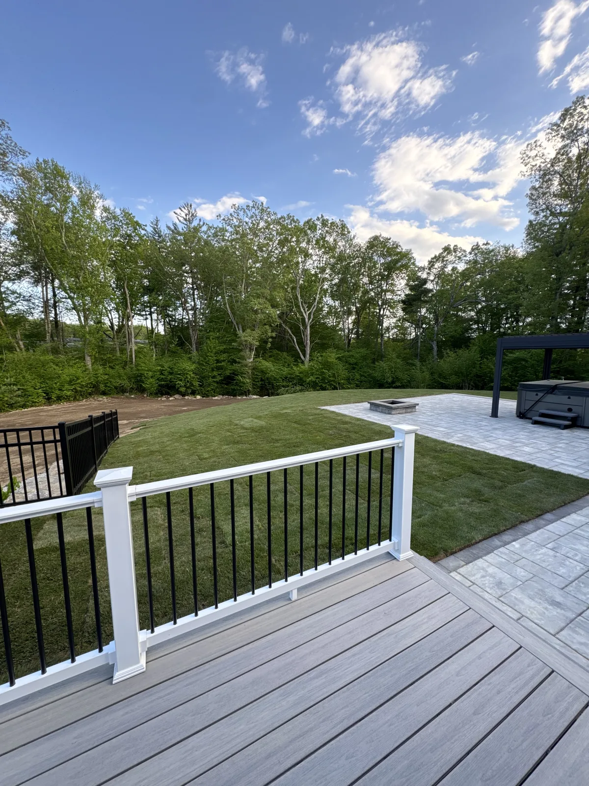 View from composite deck of completed Kentucky Bluegrass sod lawn with fire pit and hot tub on paver patio — Millbury MA